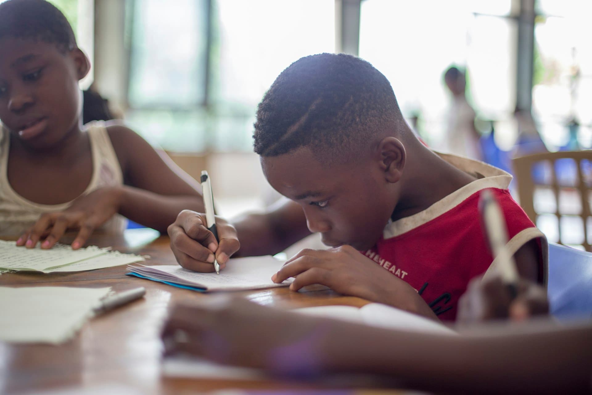 A young boy concentrating as he writes in his notebook at a classroom desk